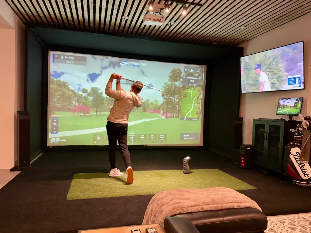 Golfer mid-swing in a residential golf simulator room, launch monitor tracking the shot